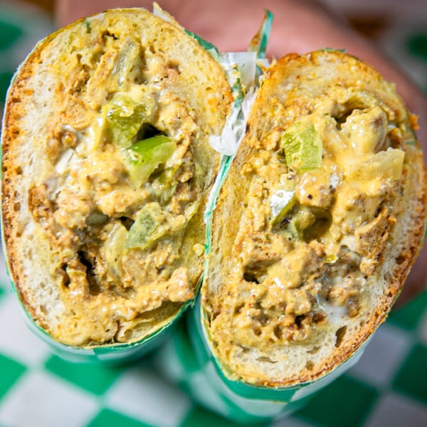 A Nishaan sandwich, cut in half, filled with creamy meat, cheese, and green peppers.