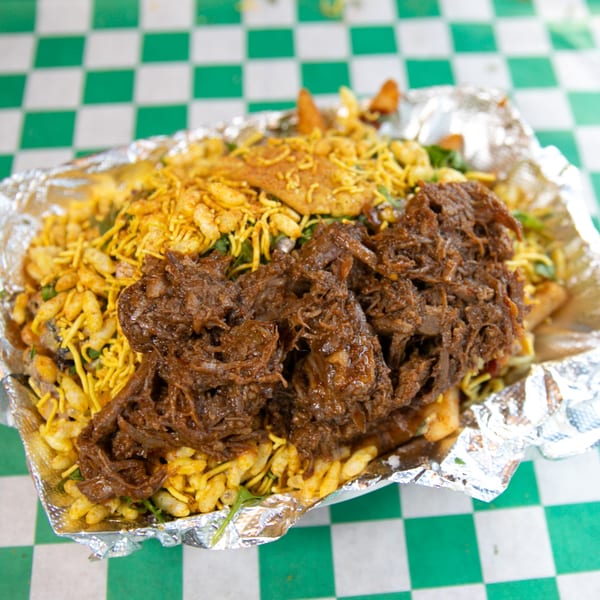 Nishaan's loaded fries with shredded meat and crispy toppings in a foil container.