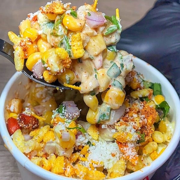A spoonful of Nishaan's elote, a Mexican street corn salad, being lifted from a white cup.