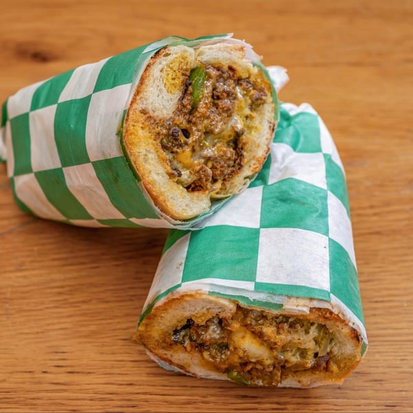 Two halves of a Nishaan sandwich, filled with meat and cheese, wrapped in green and white paper.