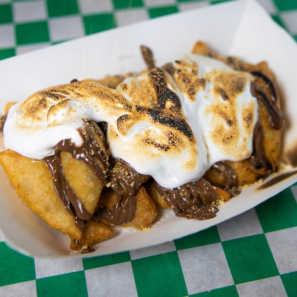 Fried dough pieces topped with melted marshmallows, chocolate sauce, and graham cracker crumbles.