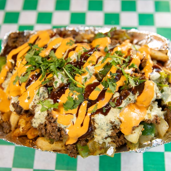 Nishaan's loaded fries with ground meat, sauces, and fresh cilantro in a foil container.