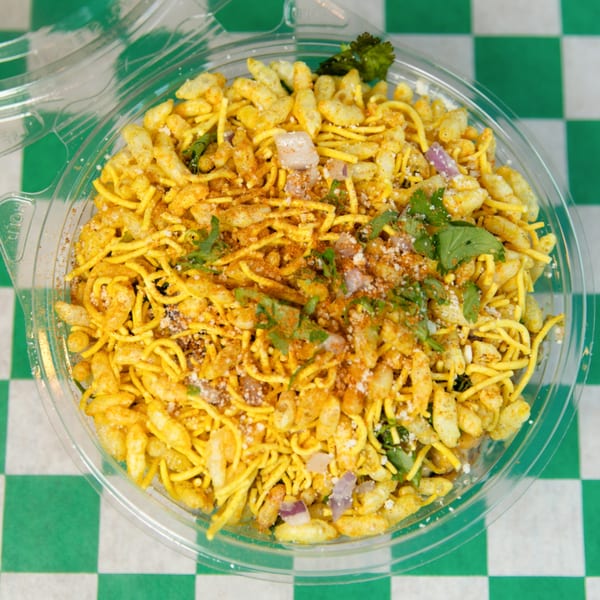 Nishaan's Bhel Puri, a savory snack with puffed rice, noodles, spices, and cilantro in a clear container.