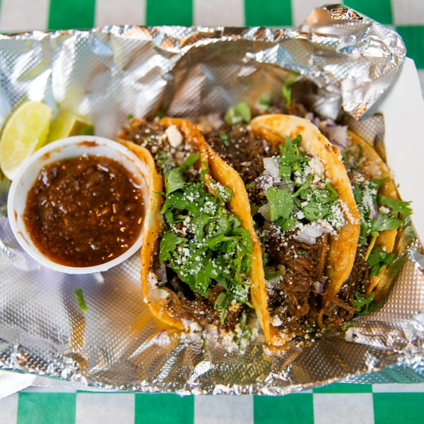 Three Nishaan tacos with meat, cilantro, cheese, and onions, served with salsa and lime wedges.