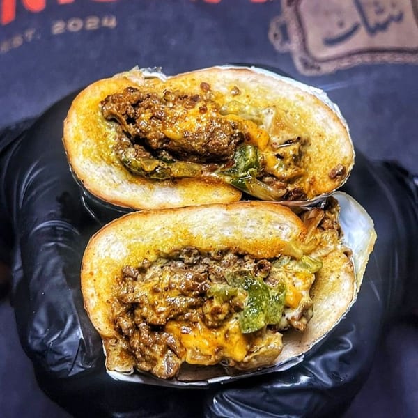 A Nishaan cheesesteak sandwich, cut in half, revealing melted cheese, meat, and green peppers.