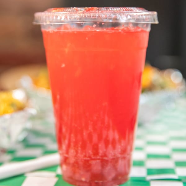 A vibrant red drink in a clear plastic cup with a lid, sitting on a green and white checkered tablecloth.