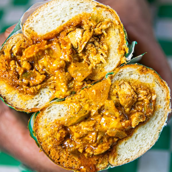 A Nishaan chicken sandwich, cut in half, revealing a rich, saucy filling with chicken pieces.
