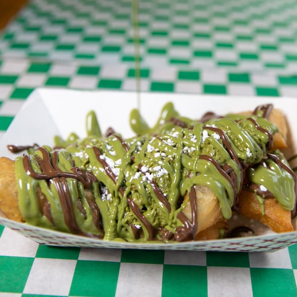 Fried pastries drizzled with green pistachio and brown chocolate sauces, dusted with powdered sugar.