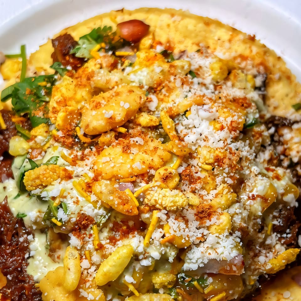 Close-up of a Nishaan sandwich, topped with crunchy snacks, white cheese, and green herbs.
