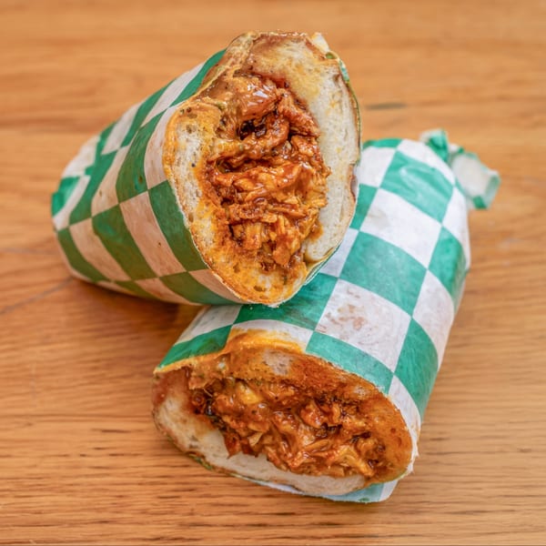 Two halves of a Nishaan sandwich, filled with saucy meat, wrapped in green and white checkered paper.