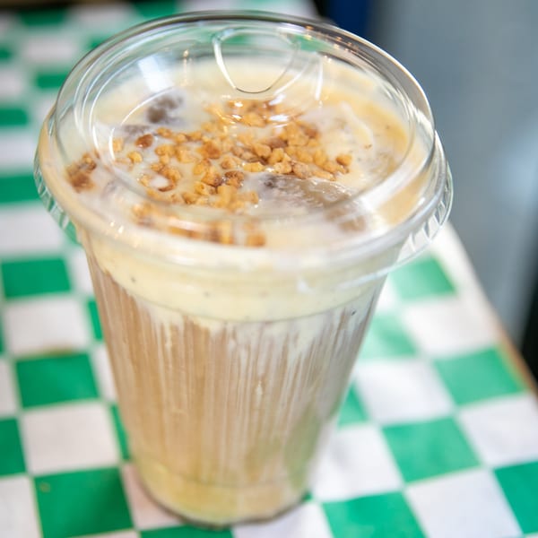 A Nishaan iced coffee with a clear lid and crunchy topping sits on a green and white checkered table.